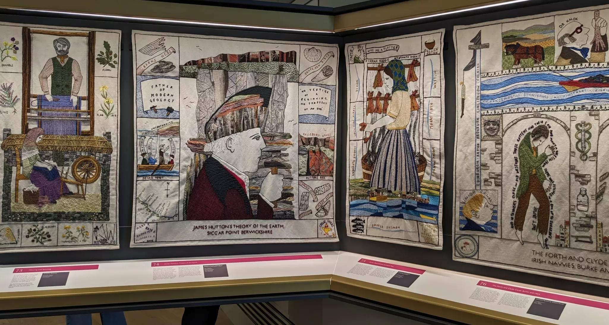 A vast tapestry depicting scenes of weavers at a loom, a man holding a hammer and a shire horse pulling a boat along a river.