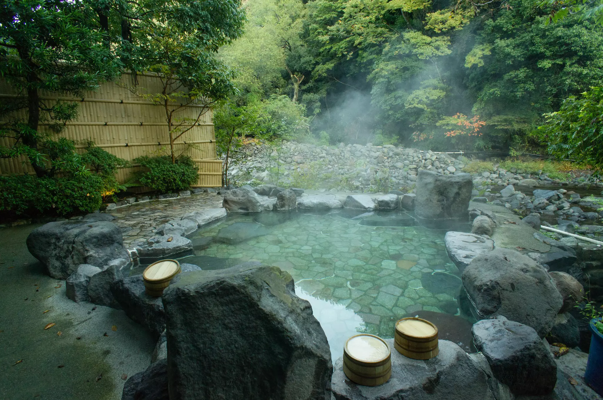 Steam rises from a hot spring pool surrounded by smooth rocks.