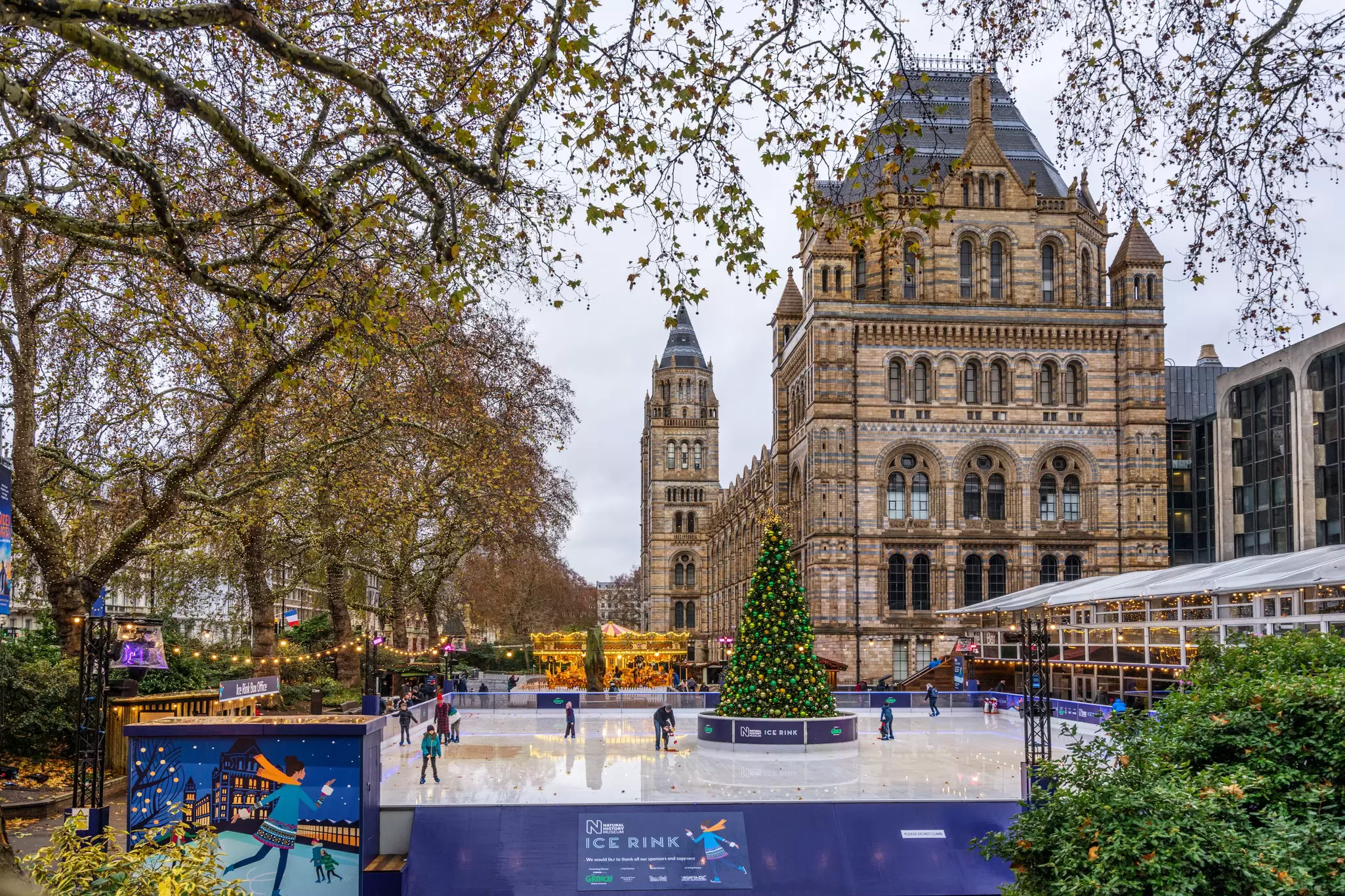 An ice rink with a Christmas tree centerpiece outside a huge Gothic style brick building