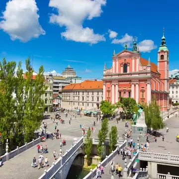 White stone bridges with balustrades crowded with walkers, a round square with a statue and a salmon-pink baroque church