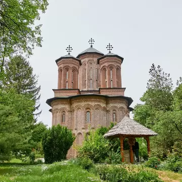 Snagov Monastery, Romania: red-brick church with three cross-topped towers and a wooden well shelter in leafy grounds
