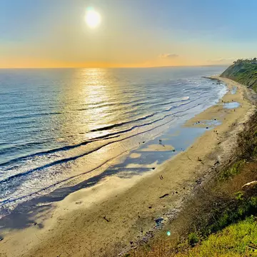 Looking down from a clifftop towards a beach with golden sand and several groups of people walking along it