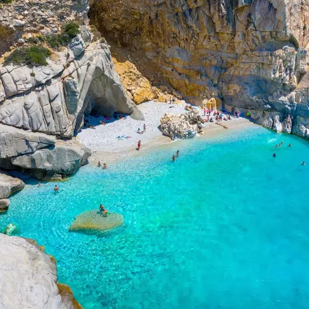 Sunny cove with brilliant blue waters, white pebble beach dotted with sunbathers and swimmers