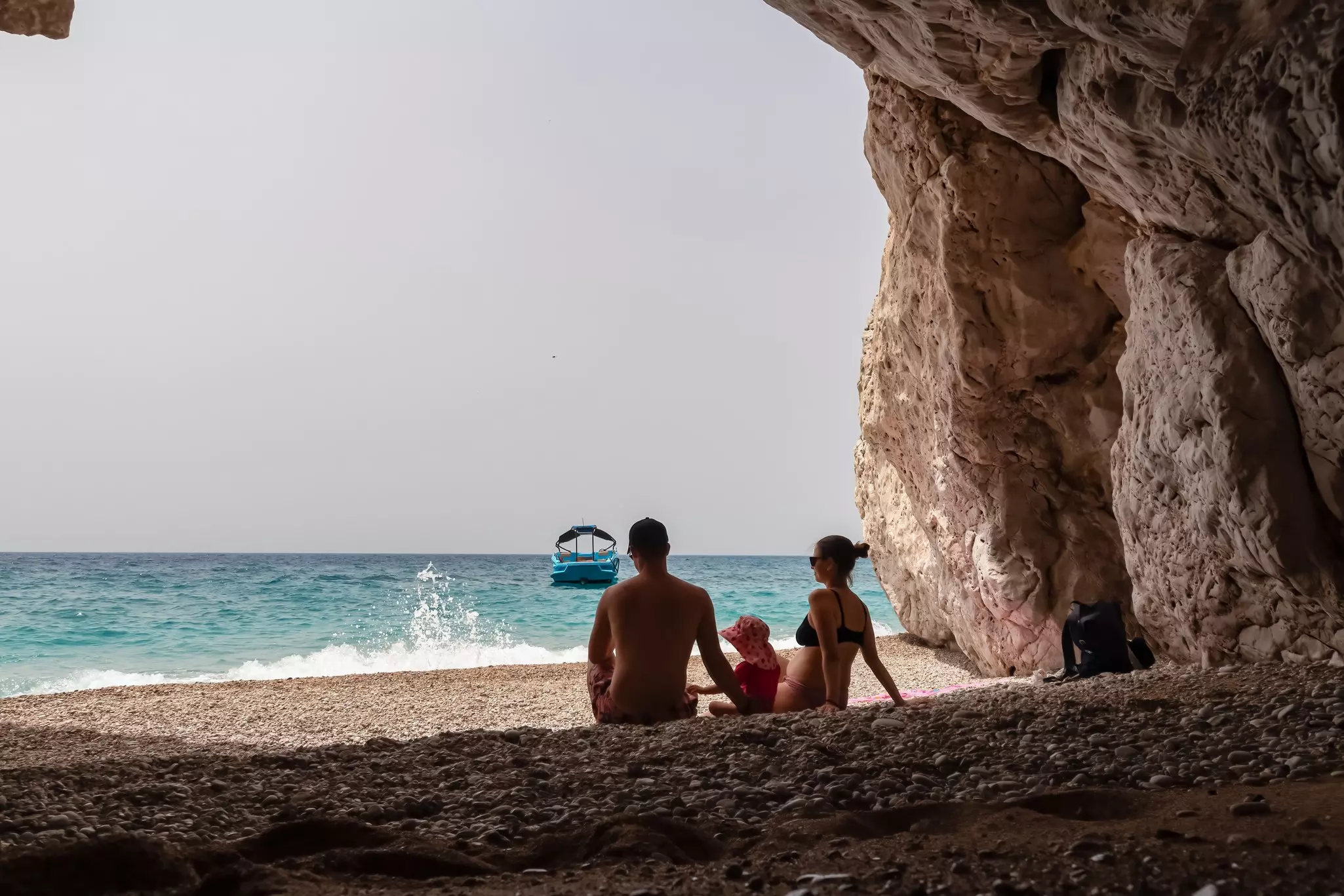 Mother and Father with small toddler sitting in idyllic cove called Pigeons Cave near Himare, Albanian Riviera, Albania.