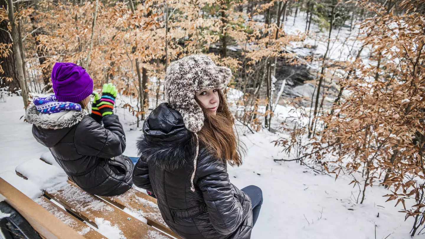 Two girls sits at the bench in the winter forest. Pennsylvania, Poconos, Austin T. Blakeslee natural are