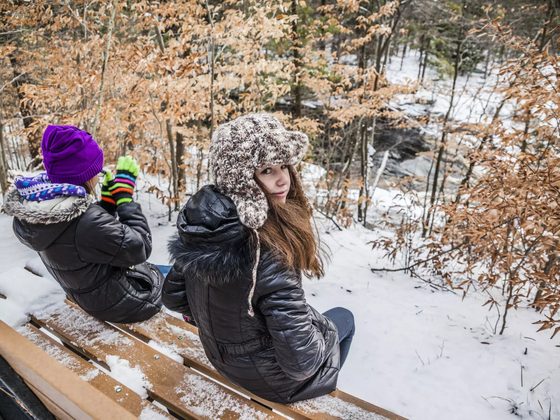 Two girls sits at the bench in the winter forest. Pennsylvania, Poconos, Austin T. Blakeslee natural are
