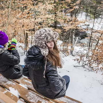 Two girls sits at the bench in the winter forest. Pennsylvania, Poconos, Austin T. Blakeslee natural are