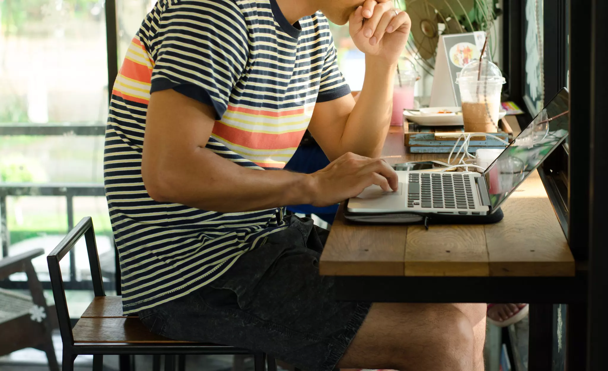 A person sitting on a stool at a cafe using a laptop