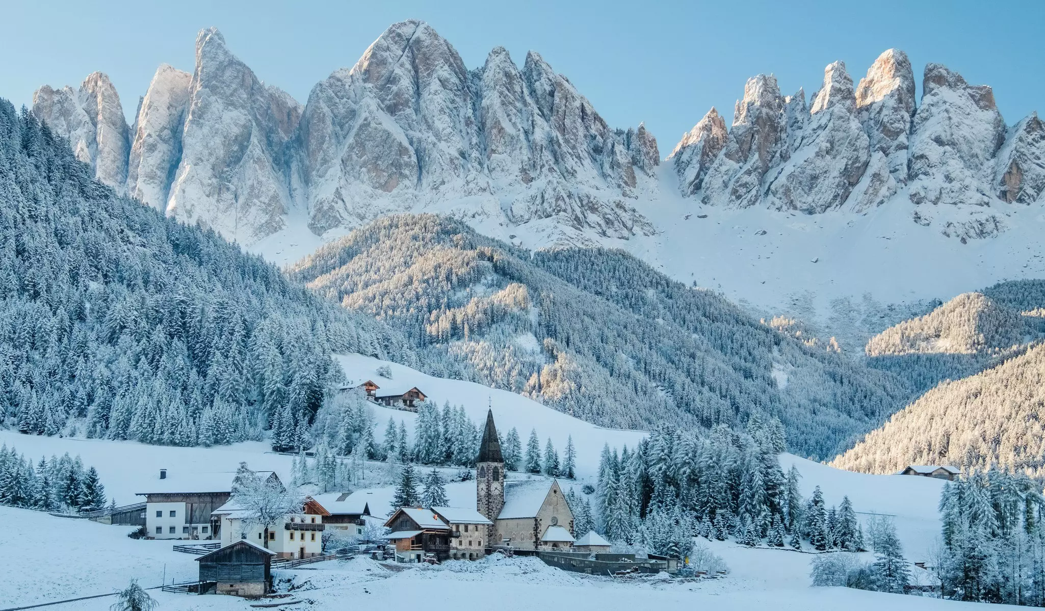 The small village of Val di Funes covered in snow, with the Dolomites mountains in the background
