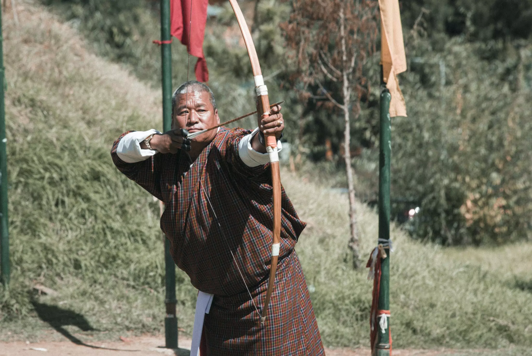 A man outdoors with a bow and arrow, presumably looking toward a target