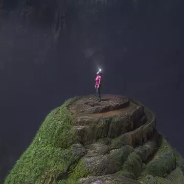 A woman wearing a helmet with a light stands at the top of a stalagmite inside Hang Son Doong cave.