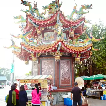 Ornate temple pavilion with colourful dragon sculptures on its roof, food carts and people standing below, Tainan, Taiwan.