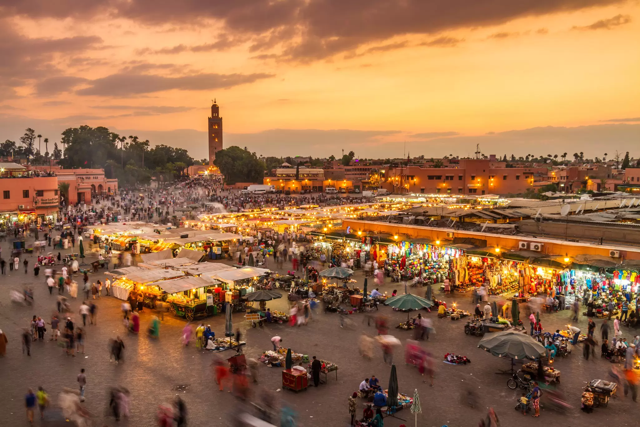 A large square with people and stalls at sunset.