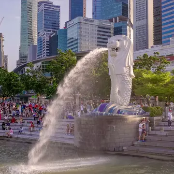 A statue shaped like a mythical beast shoots water into the harbor of a city.