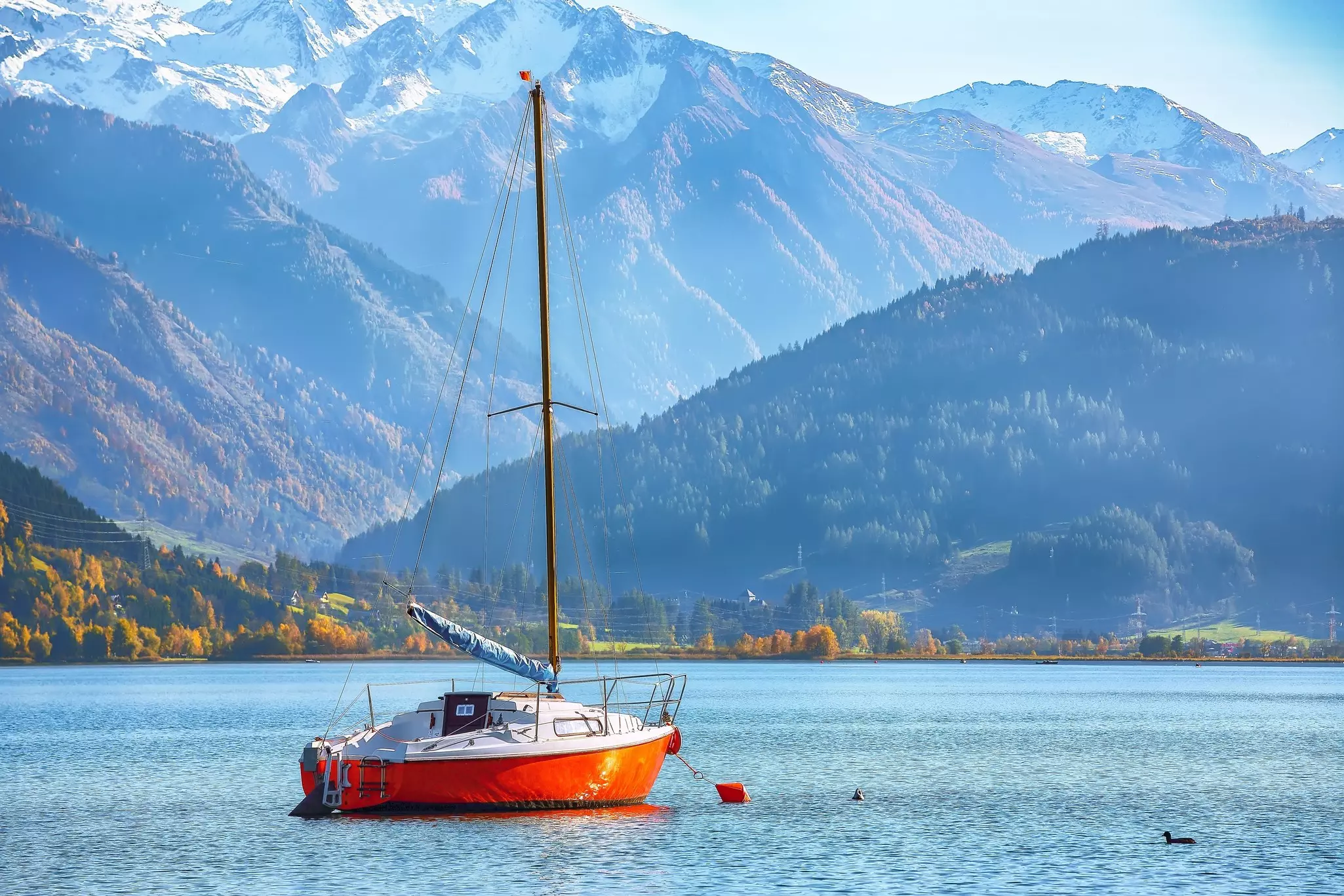 A small sailboat with a red keel on a mountain lake.
