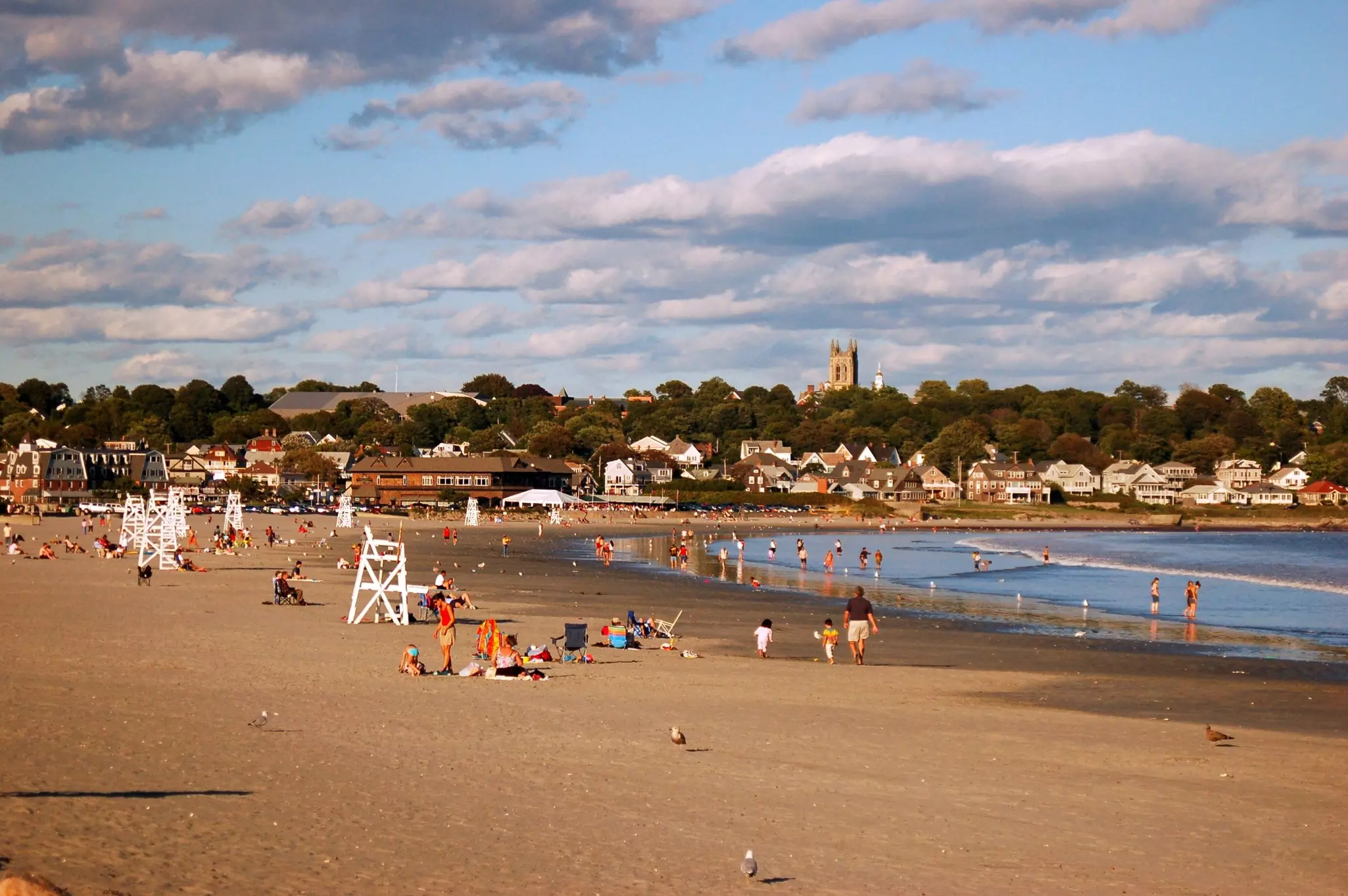 People on a sandy beach with empty white lifeguard stands.