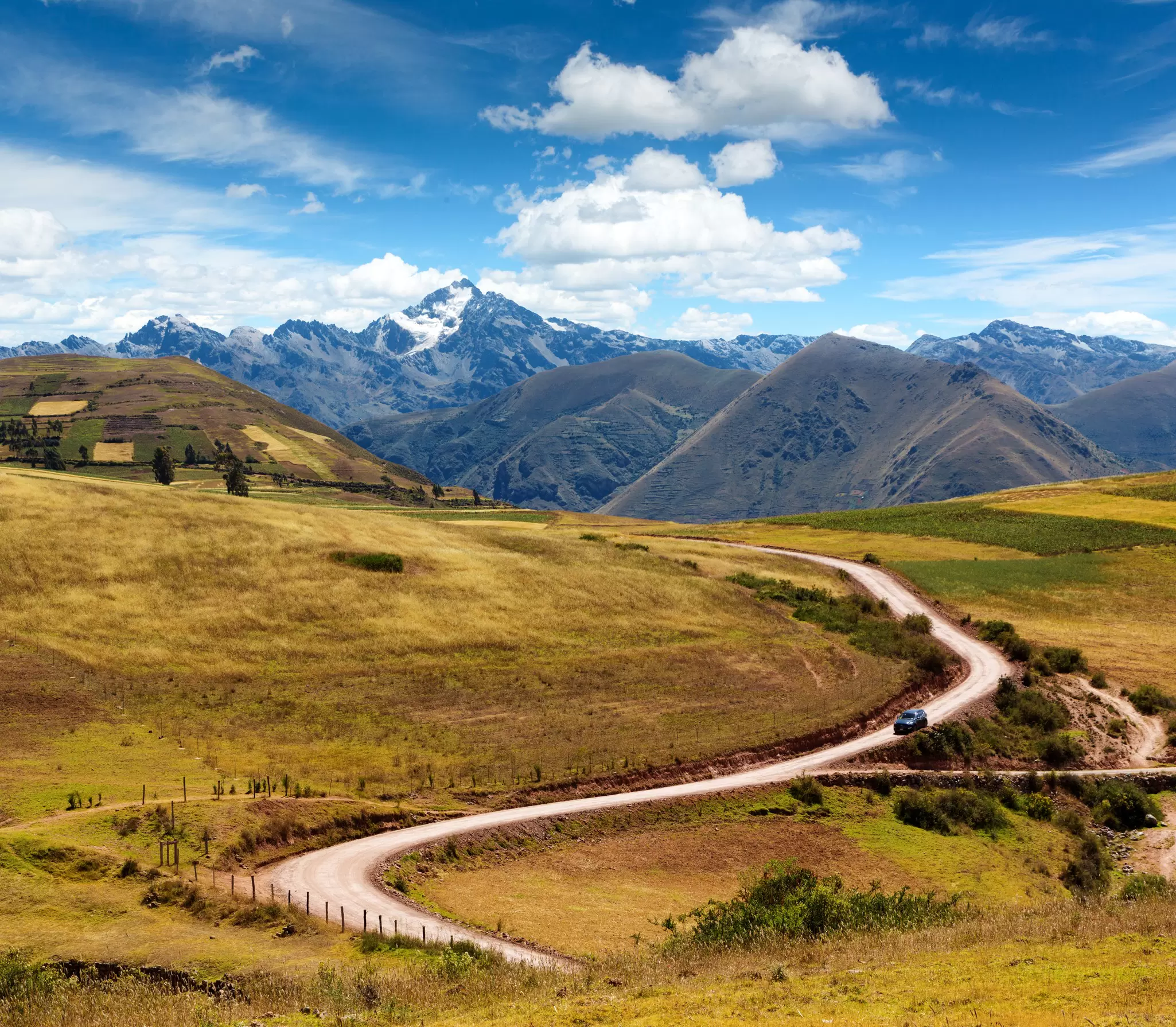 A car weaves down a road backed by mountains on a sunny day.