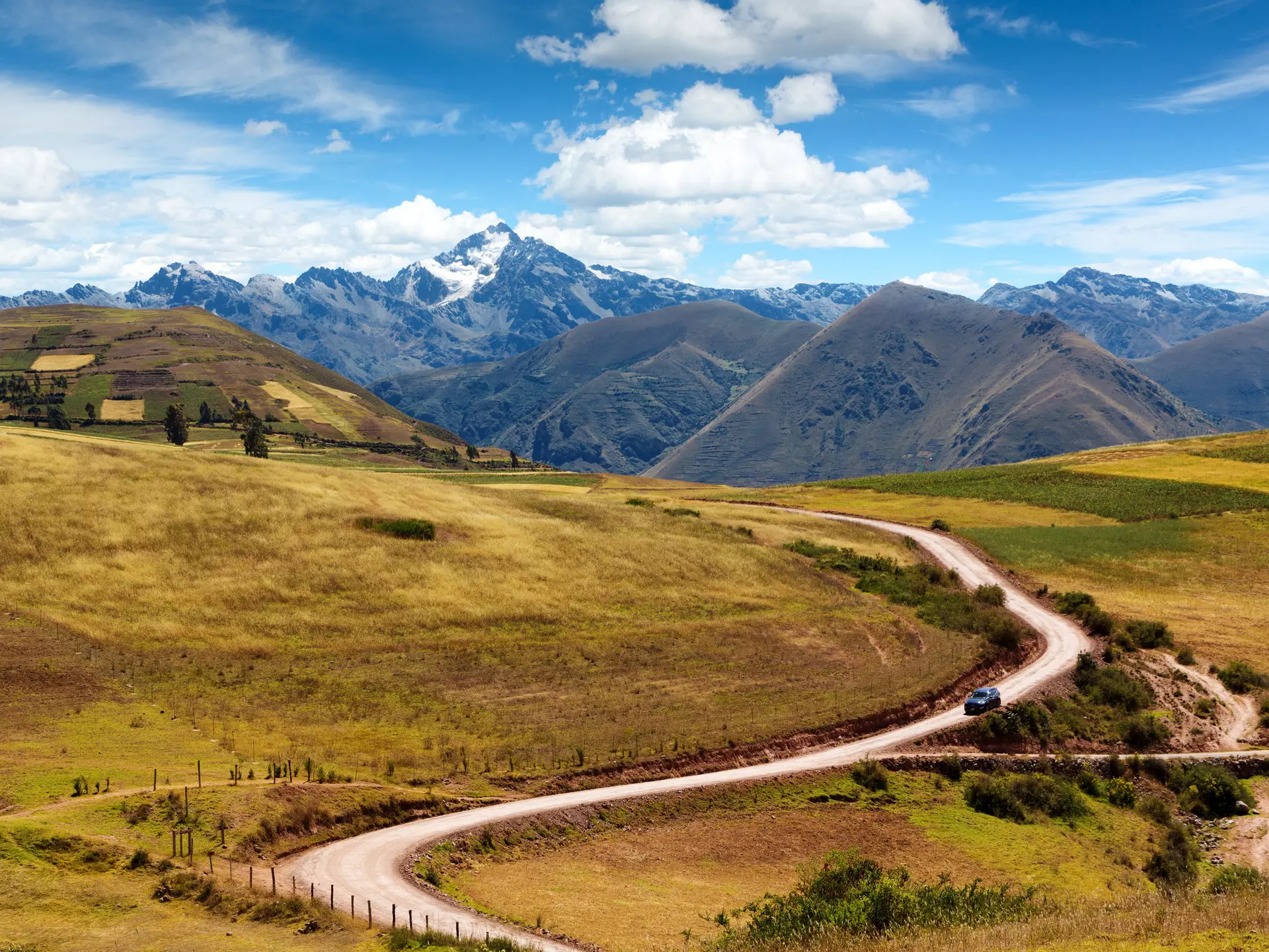 A car weaves down a road backed by mountains on a sunny day.