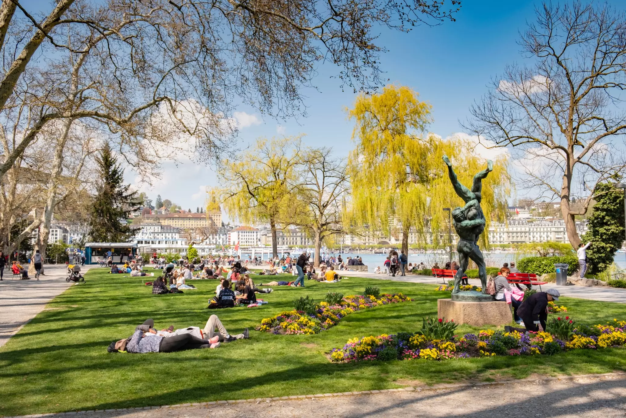 People relaxing in the park in Lucerne, Switzerland, with spring flowers and yellow trees in bloom. 