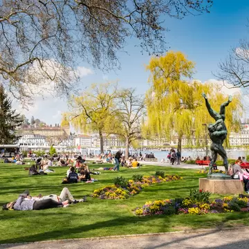 People relaxing in the park in Lucerne, Switzerland, with spring flowers and yellow trees in bloom. 
