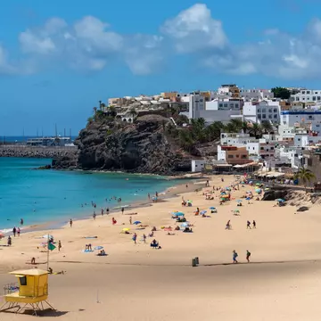 Panoramic view of the Morro Jable beach with white sand and turquoise sea full of people enjoying the sun with the village in the background the traditional architecture Fuerteventura Canary Islands, License Type: media, Download Time: 2026-03-19T18:51:27.000Z, User: jennifercarey0150, Editorial: false, purchase_order: 65050 - Digital Destinations and Articles, job: Online Editorial, client: First-timer's guide to Fuerteventura, other: Jennifer Carey
