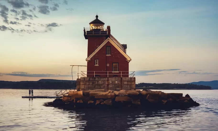 Red-brick Rockland Breakwater Lighthouse on its granite pier at dusk in Rockland Harbor, Maine, two people on a dock