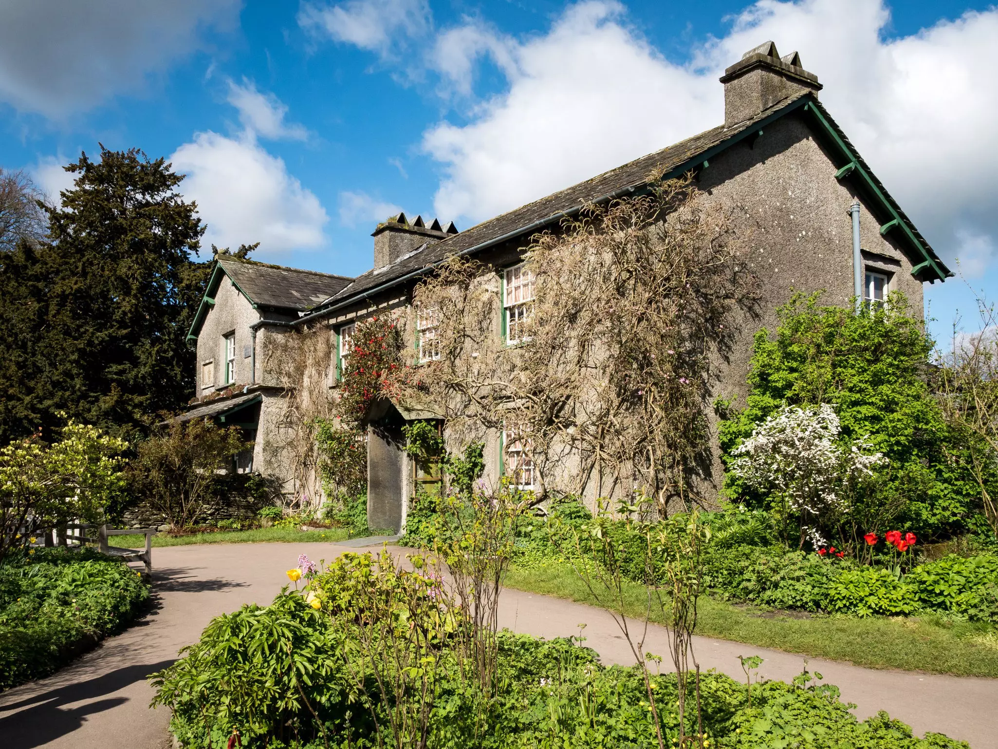 A stone house in the countryside is pictured surrounded by gardens, Near Sawrey, Lake District, England