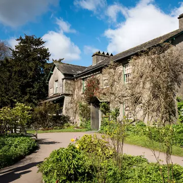 A stone house in the countryside is pictured surrounded by gardens, Near Sawrey, Lake District, England