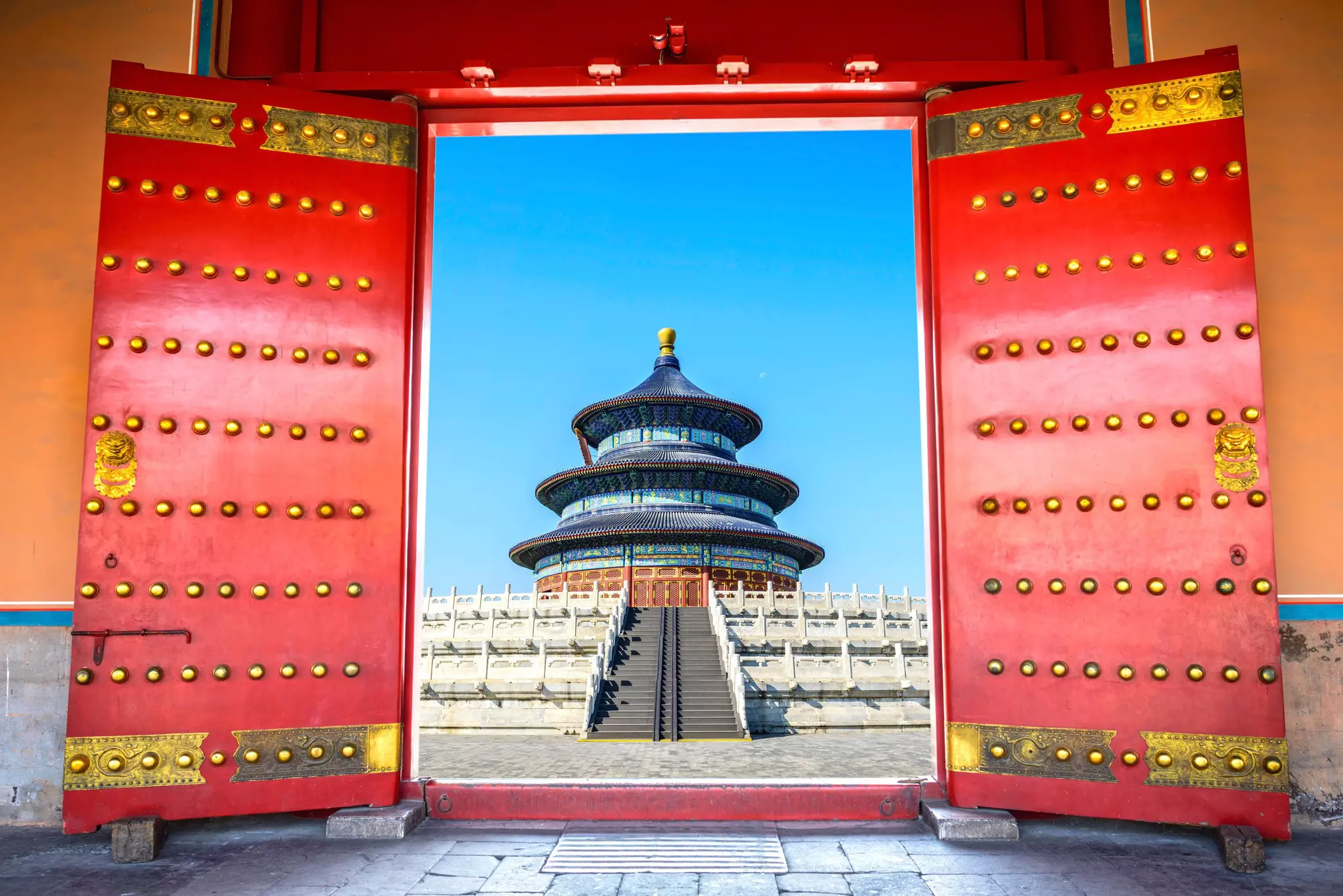 A red door leads to stairs that go up to a round temple building with blue, red, gold and turquoise tiling.