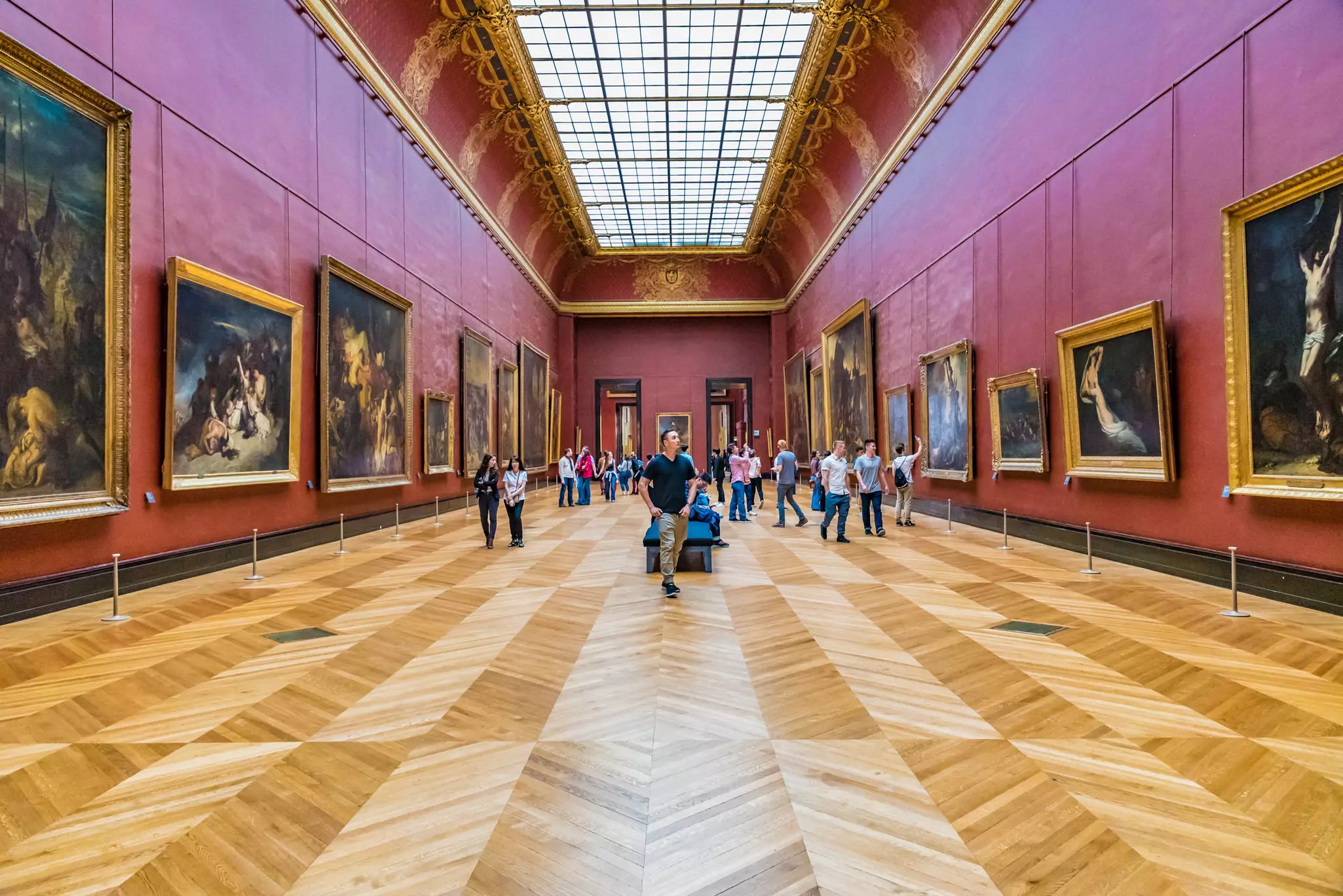 People stoll through a large hall in the Louvre, looking at art.