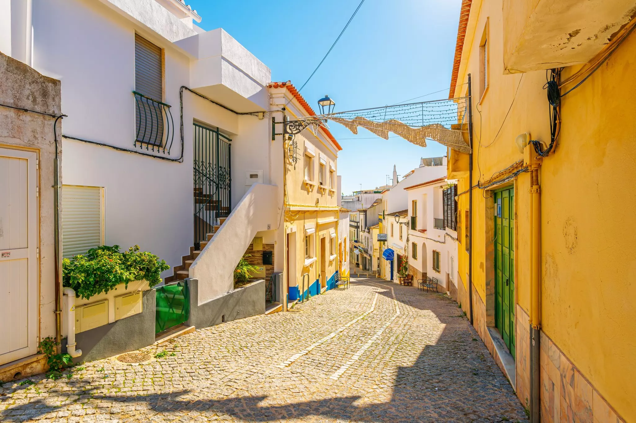 A cobbled street stretches downhill in a historic town lined with pastel-colored houses.