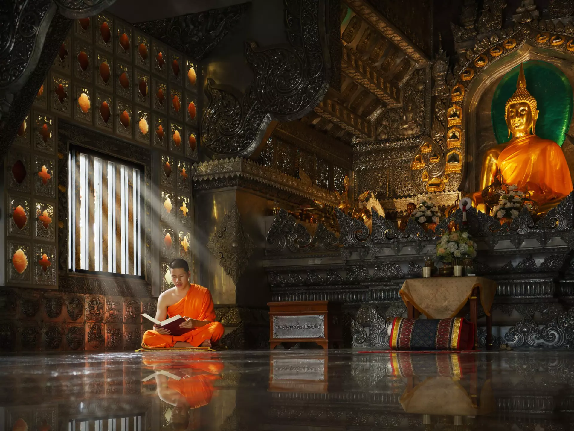 Young novice Buddhist monk, sitting cross-legged, reading inside a Chiang Mai monastery