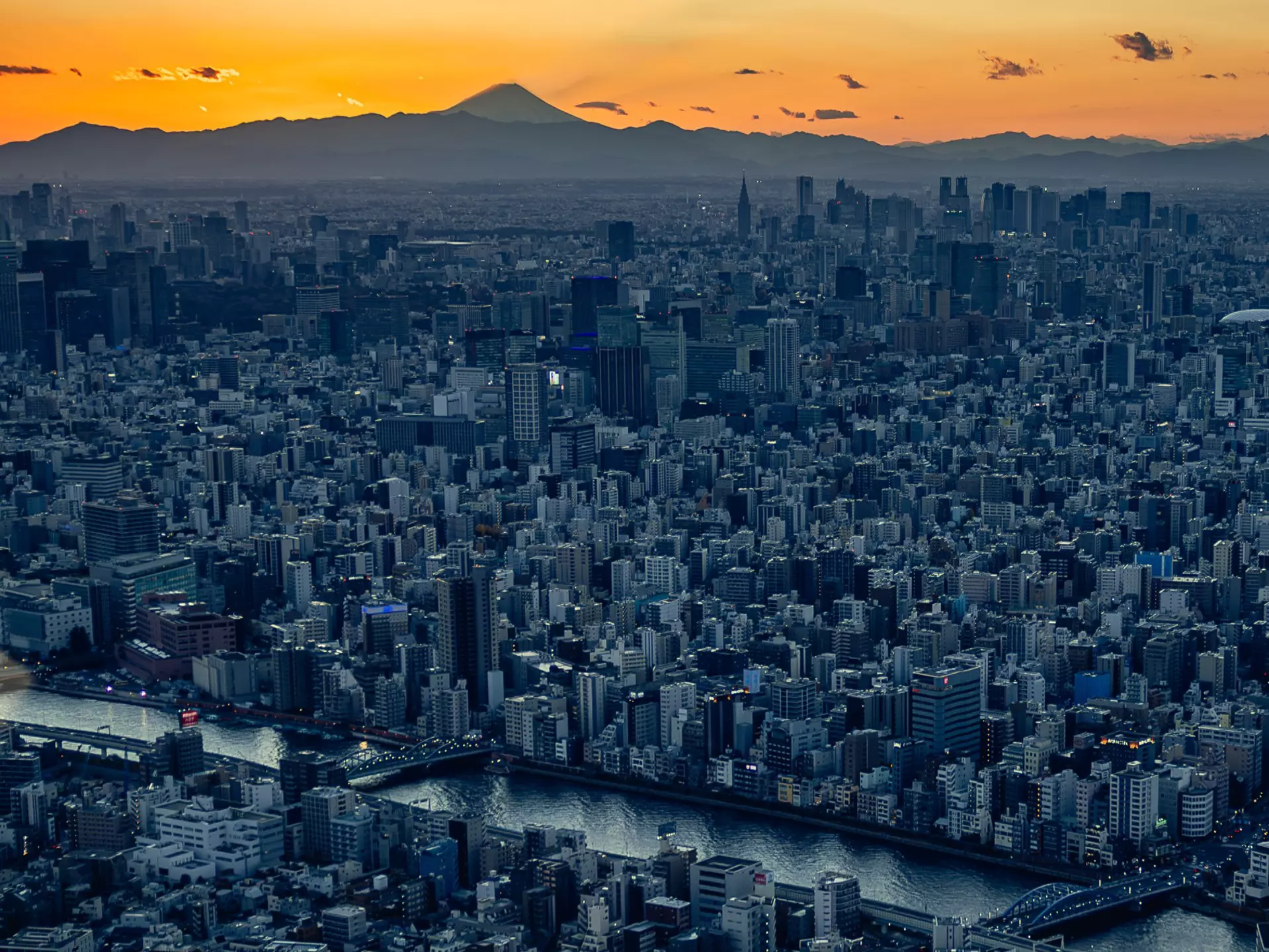 A city skyline at sunset with a distant moutain peak on the horizon. 