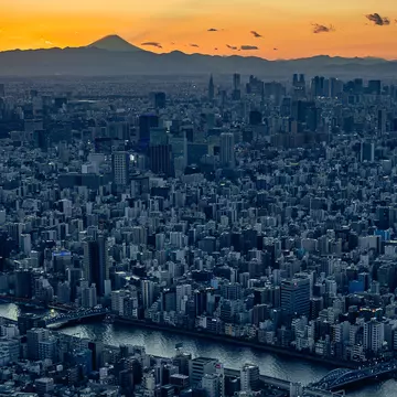 A city skyline at sunset with a distant moutain peak on the horizon. 