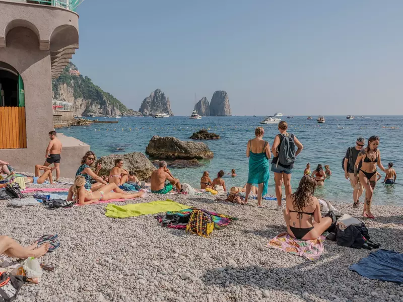 People on a beach with rocks in the water at the horizon.