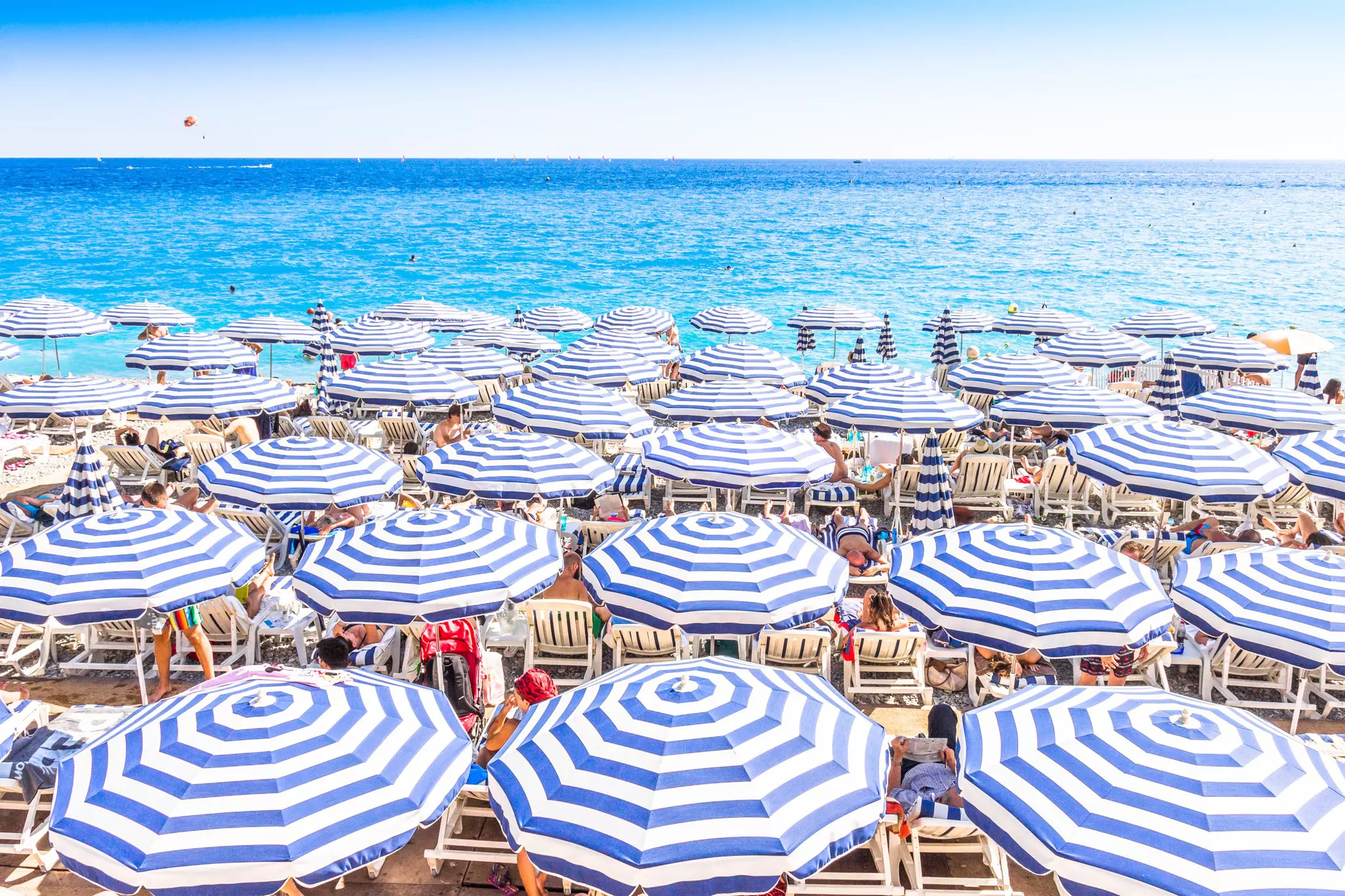 Blue-and-white-striped umbrellas give sunbathers shade on a beach in a glamorous resort town.