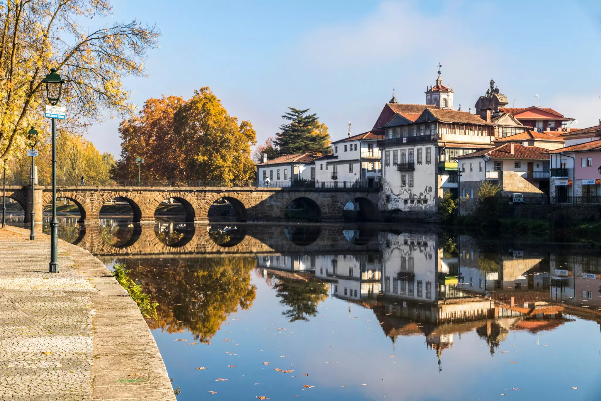 A stone bridge reflected in a calm river through a small town.