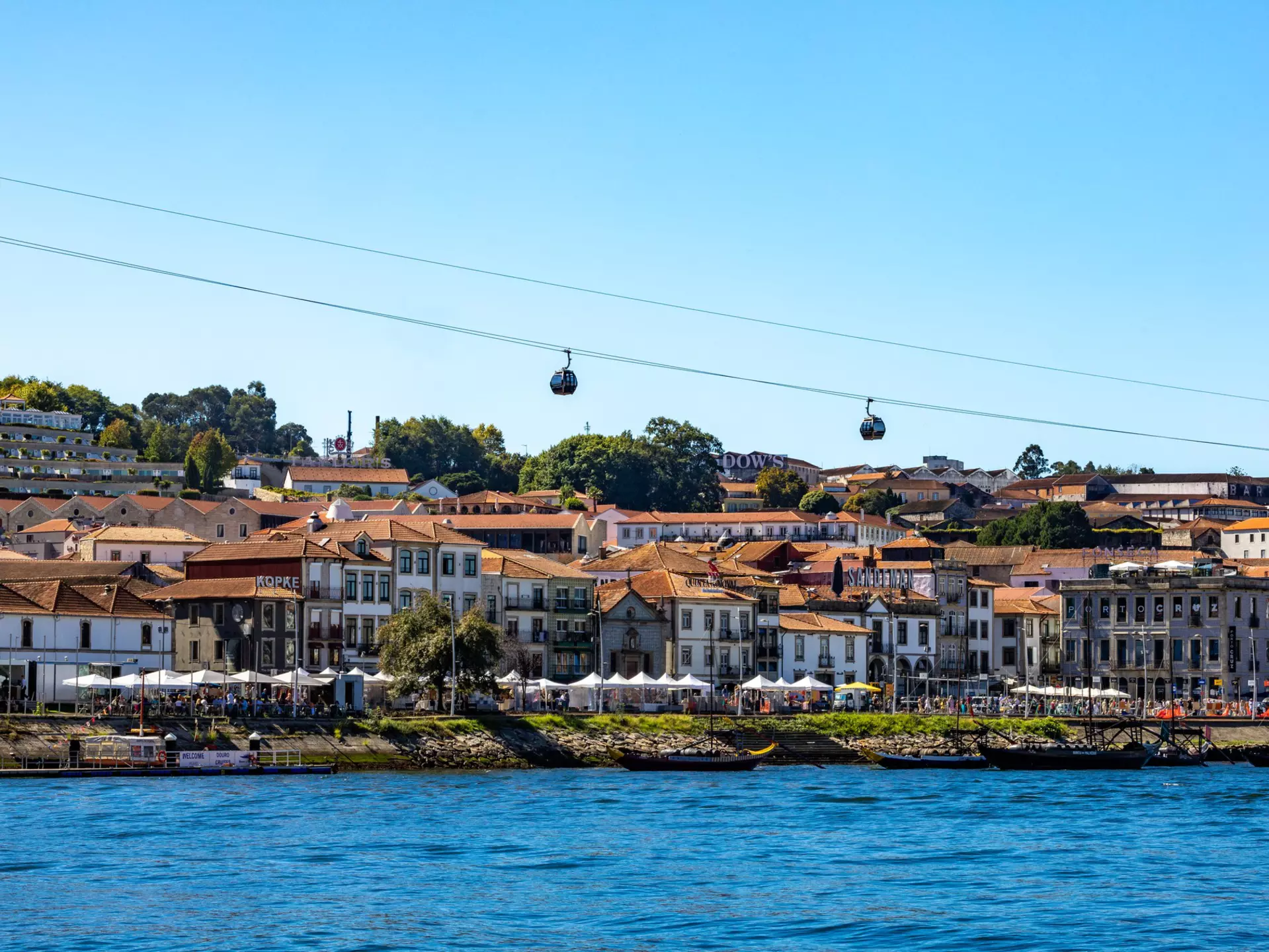 Historic riverside buildings packed tightly together. A modern cable car passes overhead.