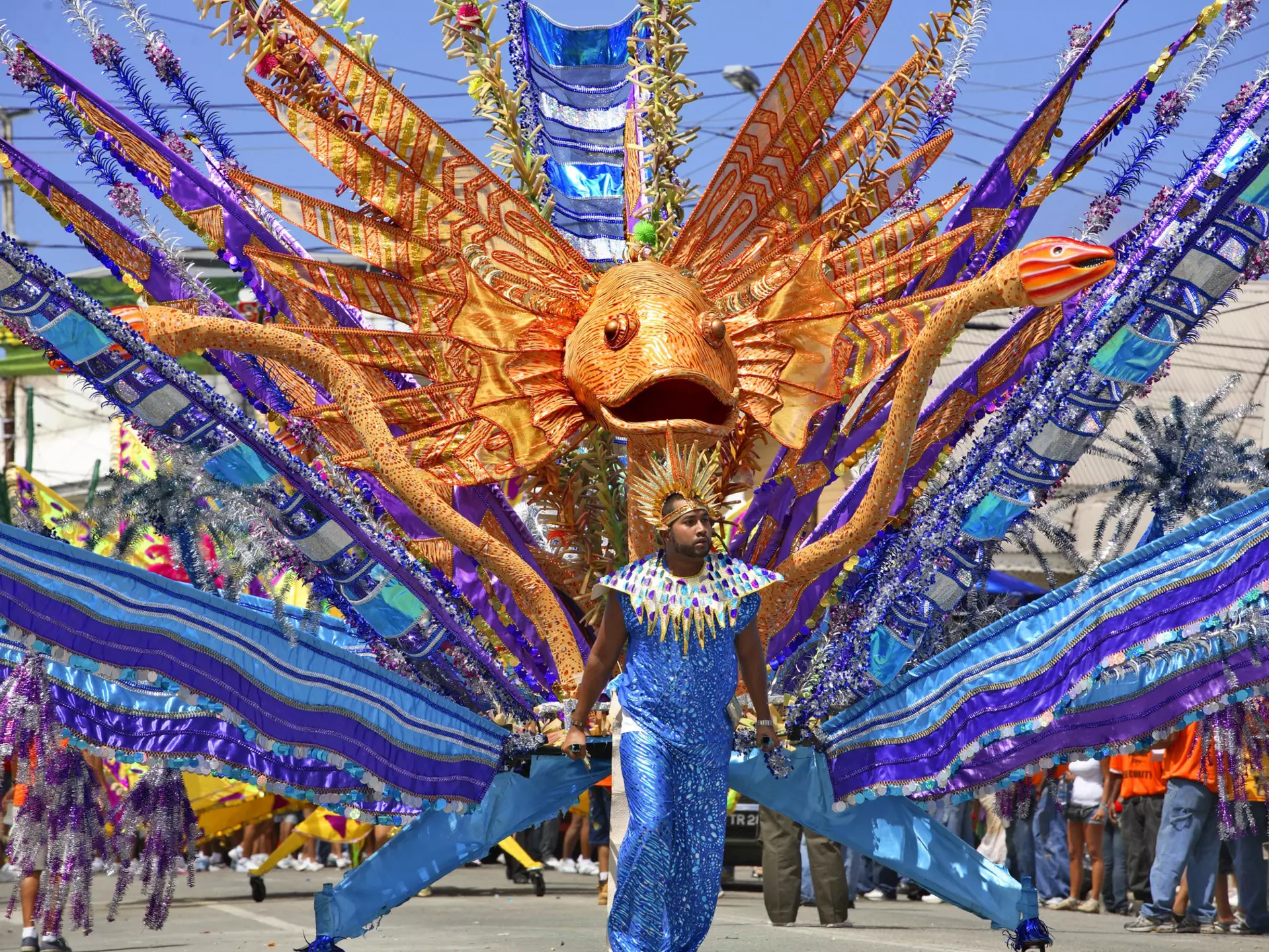 A costumed man in a Carnival parade in front of a giant fish float