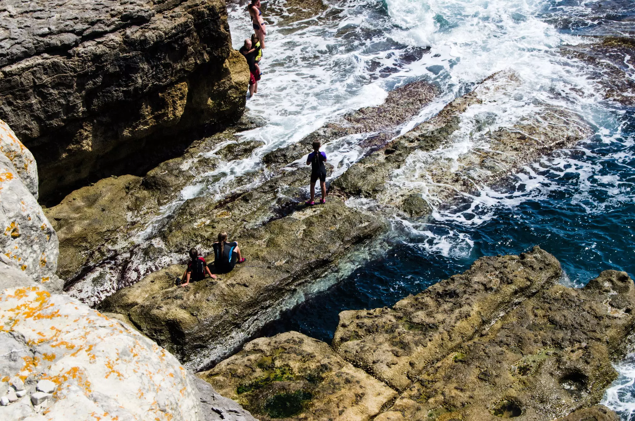 Bathers on Dancing Ledge in Dorset England on what is left of an old quarry shelf. The bathers are isolated on the shelf with the sea and rocks surrounding them.