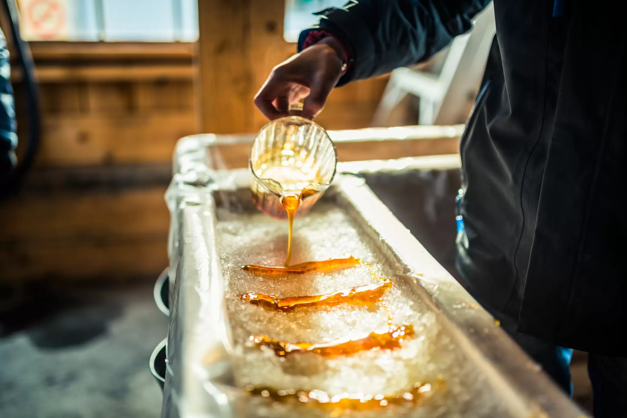 Close-up of a person at a sugar shack pouring maple syrup from a pitcher onto snow to make maple sugar taffy in Québec, Canada..