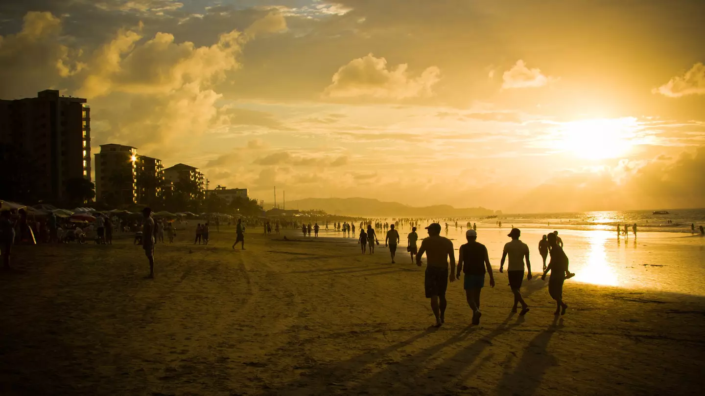Groups of people in silhouette walking on a beach as the sun sets in the sky