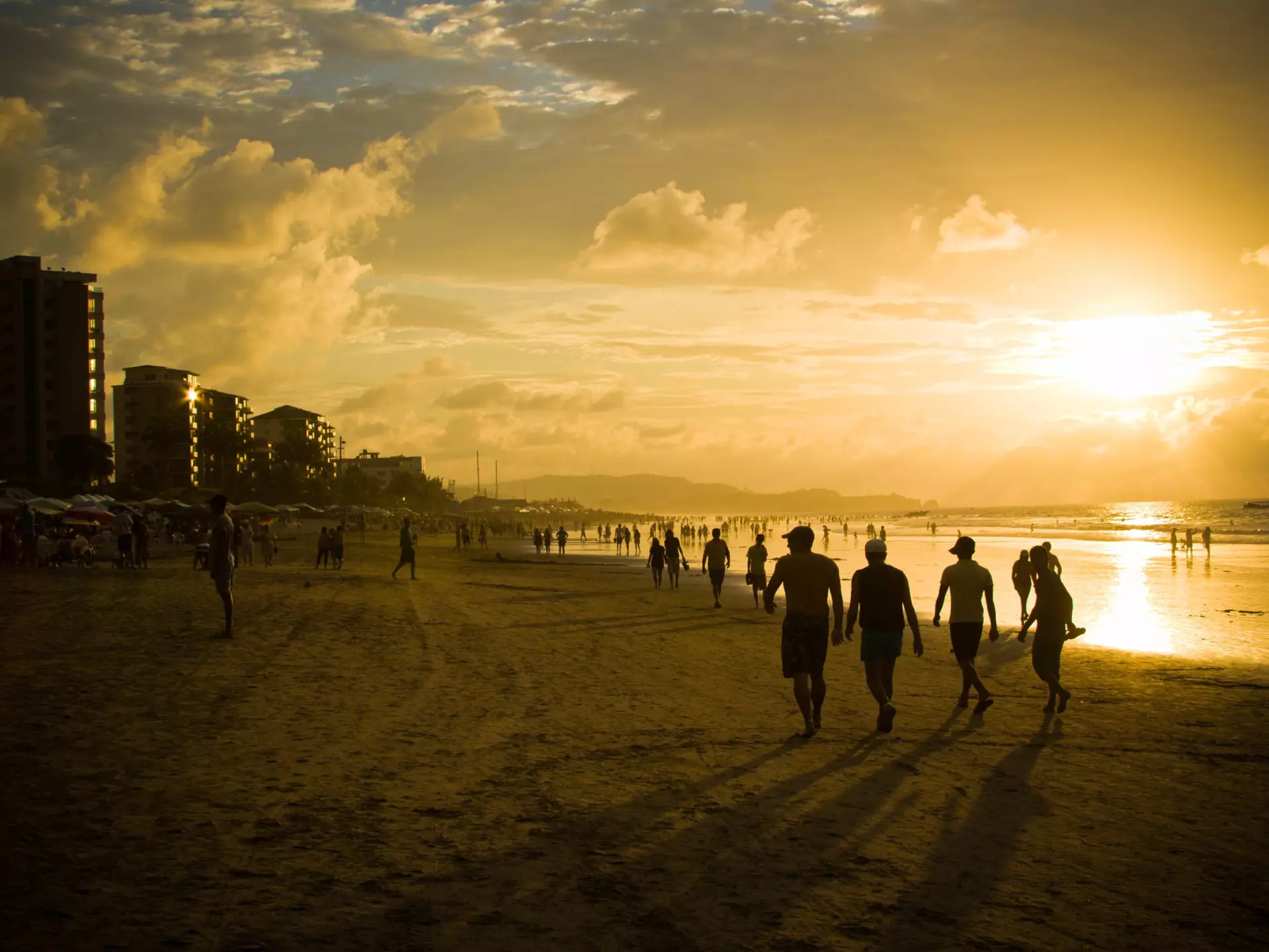 Groups of people in silhouette walking on a beach as the sun sets in the sky
