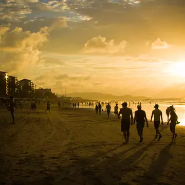 Groups of people in silhouette walking on a beach as the sun sets in the sky