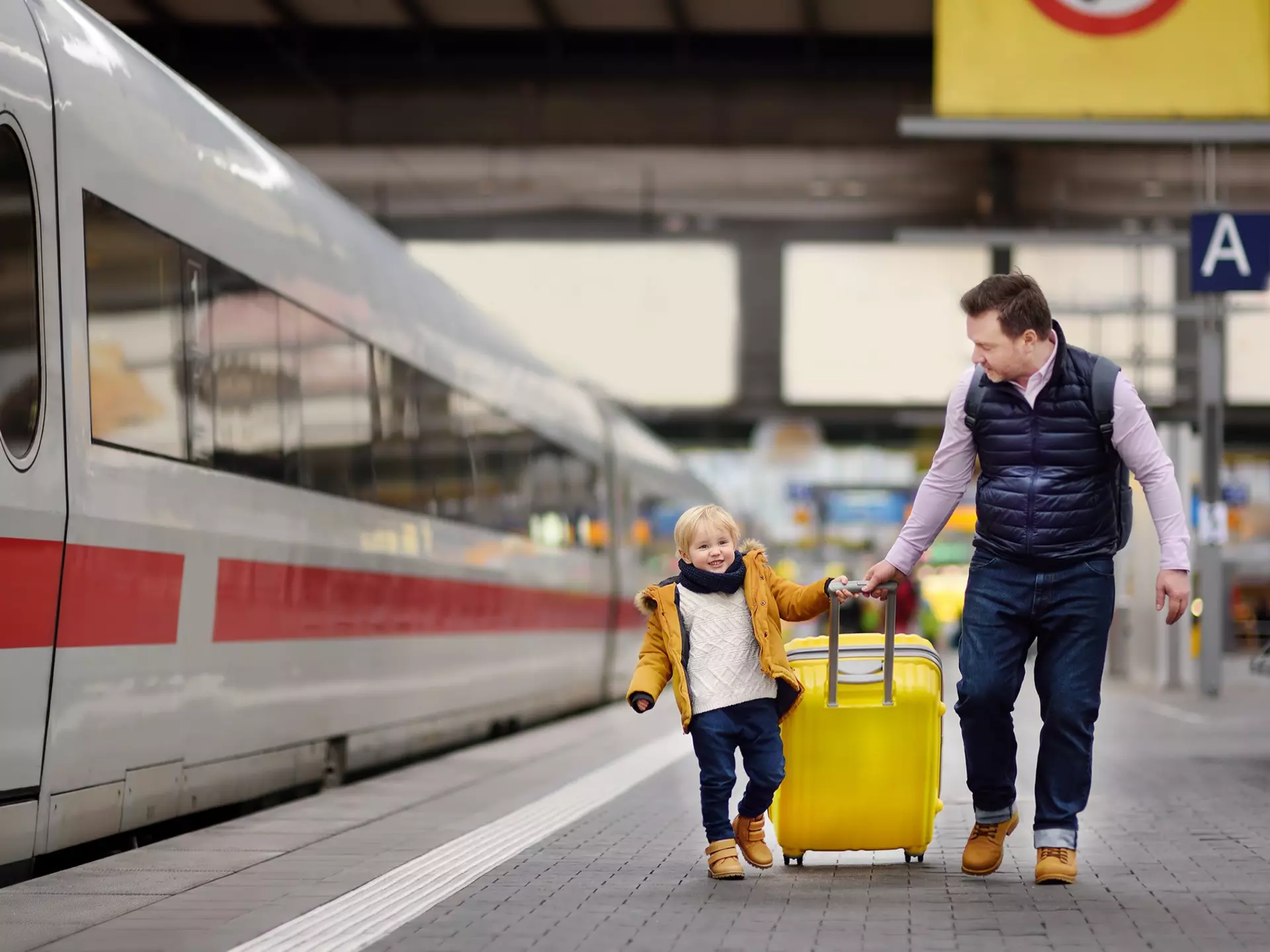 Smiling little boy and his father waiting express train on railway station platform