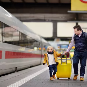 Smiling little boy and his father waiting express train on railway station platform