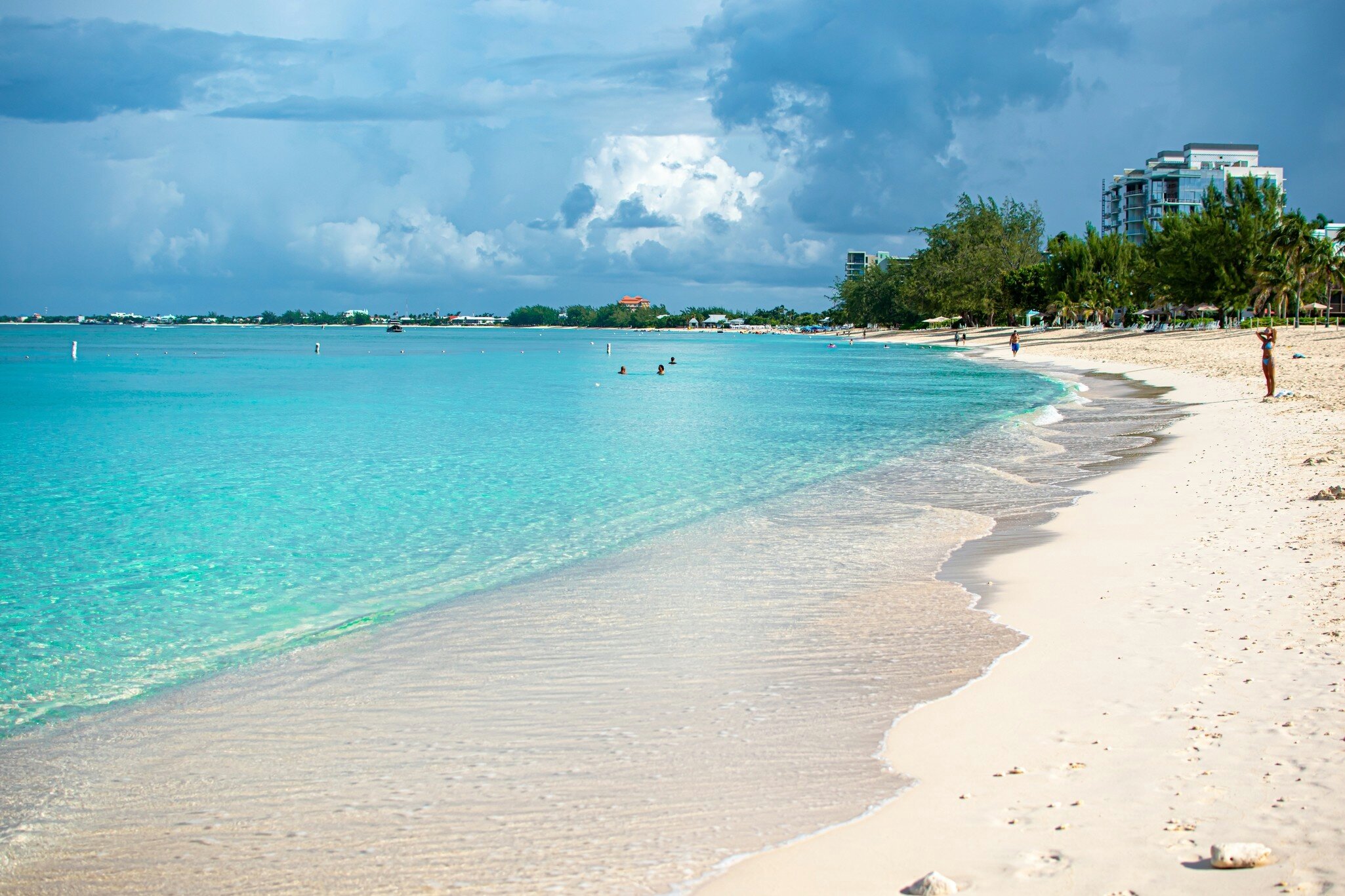 Gentle waves lap at a sandy shore as people walk along the beach.
