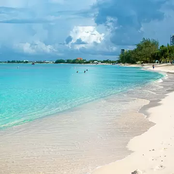Gentle waves lap at a sandy shore as people walk along the beach.
