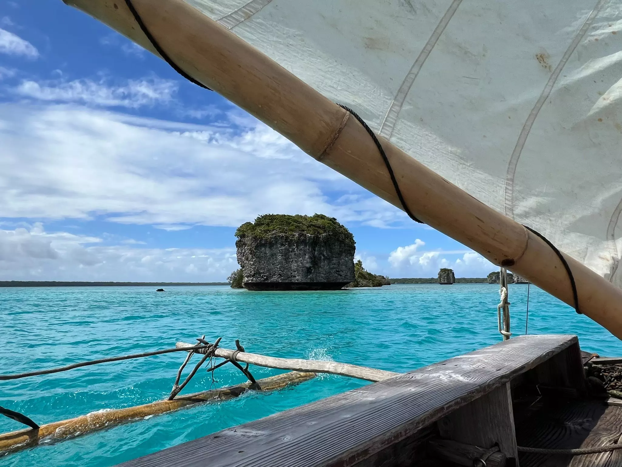 A sail boat passes an islet in a turquoise ocean.