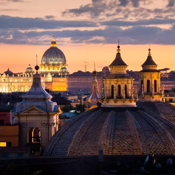 A view over the rooftops of Rome to St Peter's Basilica at sunset.